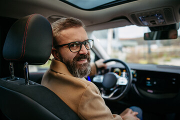 Portrait of mature man sitting in electric car, looking back over the shoulder.