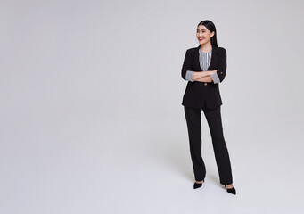 Full length portrait of an attractive asian businesswoman in suit standing with crossed arms and looking at aside isolated on gray copy space background