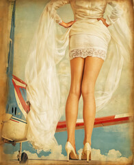 A woman with long legs and a white dress stands in front of an airplane. Vintage style