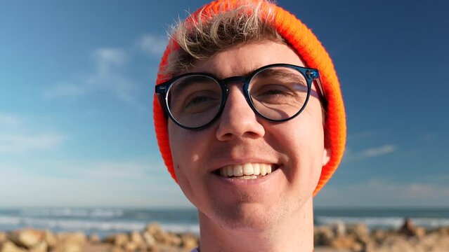 Smiling millennial man looking at camera. Happy sure handsome smart young adult, traveller posing on the beach. Close up face view portrait of joy.