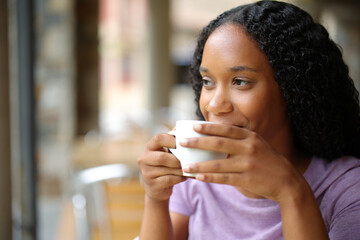 Satisfied black woman drinking coffee in a terrace