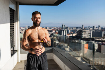 Handsome man with bare chest standing on balcony and enjoying beautiful view on city. Concept of...