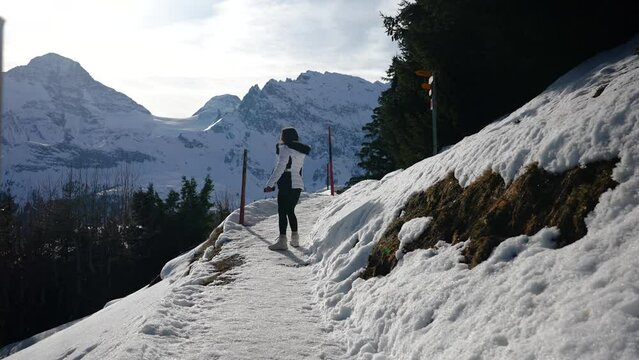 Female tourist slowly walk on narrow and snowy Switzerland mountain trail