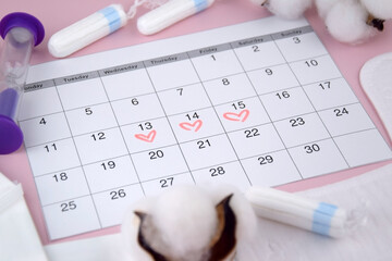Women's menstrual pads, tampons, female menstruation calendar and alarm clock on a pink background.