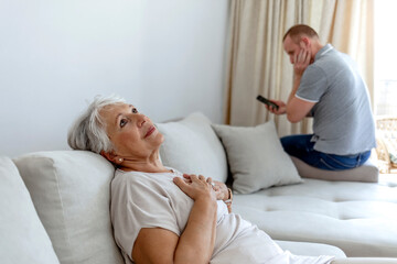 Photo of a men makes emergency call while senior women lies with heart attack at home.