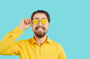 Cheerful funny hipster man in summer glasses in shape of orange slices on turquoise background. Portrait of bearded man with wide smile who is ready for summer beach party. Party accessory concept.