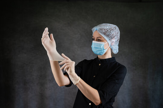Woman doctor or nurse in black uniform and protective mask putting protective glove isolatedon dark