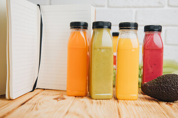 Fruit and vegetable smoothies in transparent plastic bottles. Green, red, orange smoothies on a green and wooden background. The concept of healthy eating. Front view