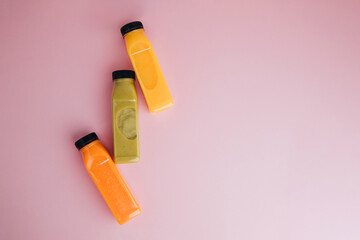Fruit and vegetable smoothies in transparent plastic bottles. Green, orange smoothies on a pink...