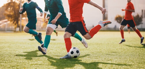 Adult Football Soccer Players Running with Ball. Footballers Kicking Play League Match During Sunny Day. Two Teams in Sport Competition. Teenage Soccer Players Running in a Duel and Kicking Ball