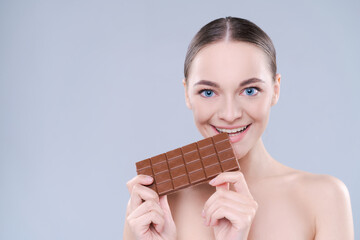 Close up beautiful girl biting chocolate bar joyfully on white background, studio shot.