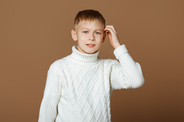 Portrait of disappointed teen boy, frowning and looking upset, wearing white knitted sweater, beige studio background