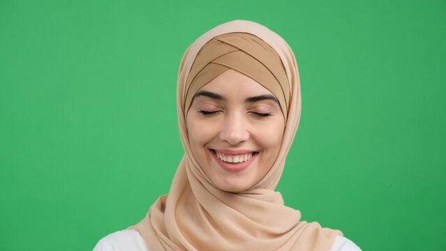 Close up portrait of a happy and smiling Arabian woman over green background. Young satisfied muslim woman in traditional hijab looking at camera. Eastern individuality, positive woman.