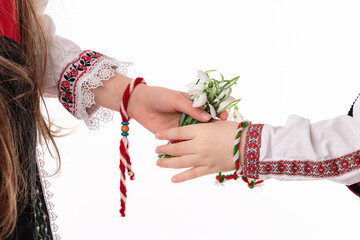 Bulgarian kids boy and girl in traditional ethnic folklore costumes with hands with bouquet of spring flowers snowdrops and handcraft wool bracelet martenitsa symbol of Baba Marta March holiday - 728413927