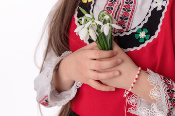 Bulgarian girl in ethnic folklore embroidery dress nosia, yarn bracelet martenitsa, and spring bouquet snowdrops symbol of Bulgaria - 728414134