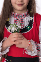 Bulgarian girl in traditional folklore costumes with spring flower bouquet snowdrops and handcraft wool bracelet martenitsa symbol of Baba Marta and march - 728414174