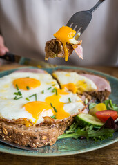 Close up of fried eggs and ham on brown bread on a plate being eaten on a wooden table in café restaurant