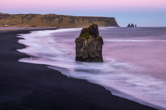 Scenic pink sunset at Dyrholaey cliff in Iceland with sea stack views and waves on Reynisfjara black sand beach