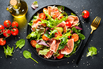 Salad in black bowl at dark background.