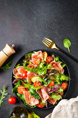 Salad in black bowl at dark background.
