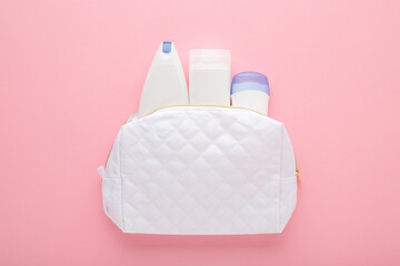 White cosmetic travel bag with plastic bottles on light pink table background. Pastel color. Care about clean and body skin. Female beauty products. Closeup. Top down view.