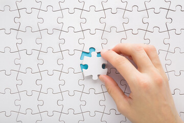 Young adult woman hand holding and putting last one white puzzle piece in middle on blue table...