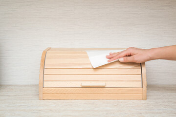 Young adult woman hand holding dry white paper napkin and wiping wooden bread box on table top at...