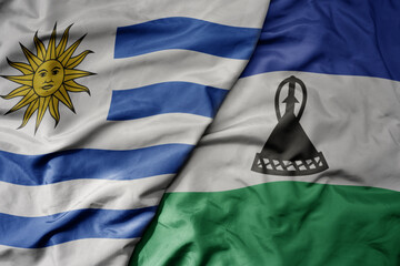 big waving national colorful flag of lesotho and national flag of uruguay .