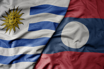 big waving national colorful flag of laos and national flag of uruguay .