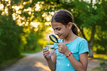 A child looks into a glass of water with a magnifying glass. Selective focus.