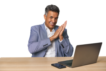 Elegant businessman at desk with laptop feeling energetic and comfortable, rubbing hands confident.