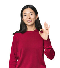 Young Chinese woman in studio setting cheerful and confident showing ok gesture.