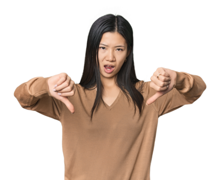 Young Chinese woman in studio setting showing thumb down and expressing dislike.