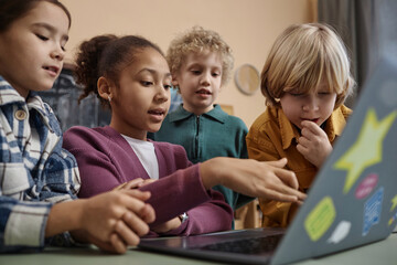 Diverse group of school children looking at computer screen together watching online presentation