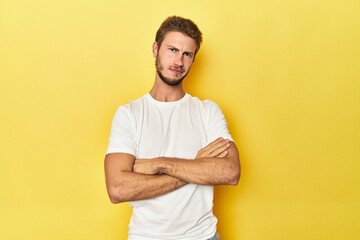 Young Caucasian man on a yellow studio background suspicious, uncertain, examining you.