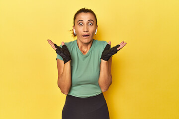 Athletic middle-aged woman on yellow backdrop surprised and shocked.