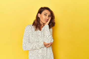 Middle-aged woman on a yellow backdrop who is bored, fatigued and need a relax day.