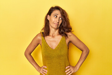 Middle-aged woman on a yellow backdrop confused, feels doubtful and unsure.