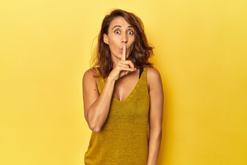 Middle-aged woman on a yellow backdrop keeping a secret or asking for silence.