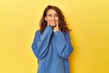 Middle-aged woman on a yellow backdrop doubting between two options.
