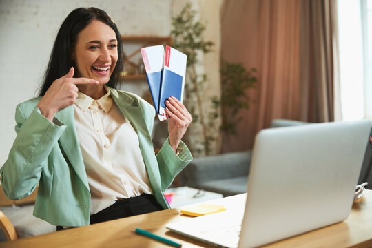 Happy, emotional businesswoman sitting in her office, talking on video call and showing plane tickets. Long awaited vacation. Concept of traveling, online services for booking, tourism, vacation