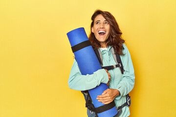 Middle aged woman with mountain backpack and mat on yellow