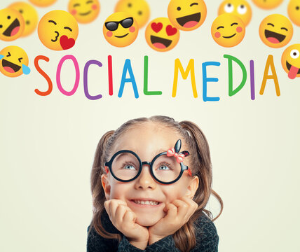 Beautiful cute little girl with eyeglasses leaning on table and looking at group of emojis and Social Media text above her head.