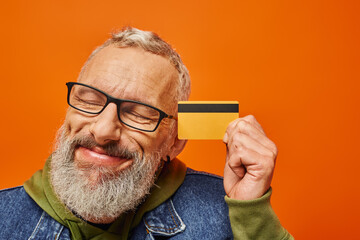 handsome mature male model in vibrant clothing posing with closed eyes and holding credit card