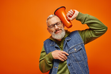 cheerful good looking mature man in vibrant attire posing with closed eyes with megaphone near head