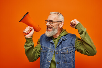 cheerful handsome mature male model in vibrant outfit posing with megaphone and looking away