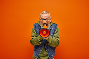 Fototapeta premium funky attractive mature man in stylish denim vest talking into megaphone and looking at camera