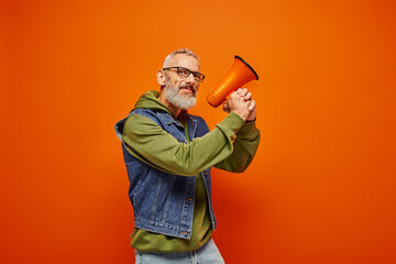 funky cheerful mature male model with beard and glasses posing with megaphone and looking at camera