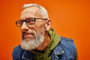 cheerful handsome mature male model with glasses posing on orange backdrop and looking ta camera