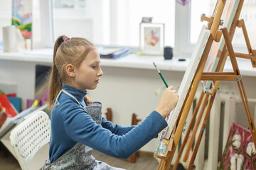 Focused student carefully sketching initial outlines of drawing on blank canvas in an art class...